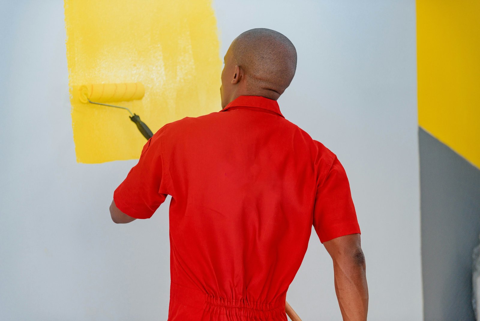 Maler in roter Arbeitskleidung streicht eine Wand mit der Farbrolle
